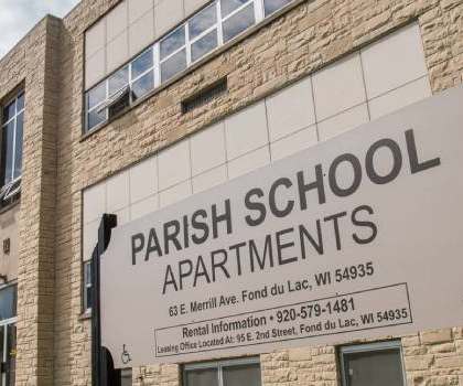 A sign for Parish School Apartments is displayed in front of a building.