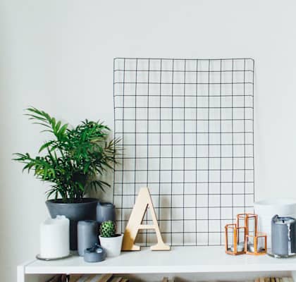 A white shelf with a plant, candles, and decorative items.