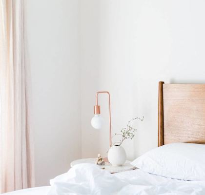 A bedroom with a bed, a nightstand with a lamp, and a window with curtains.