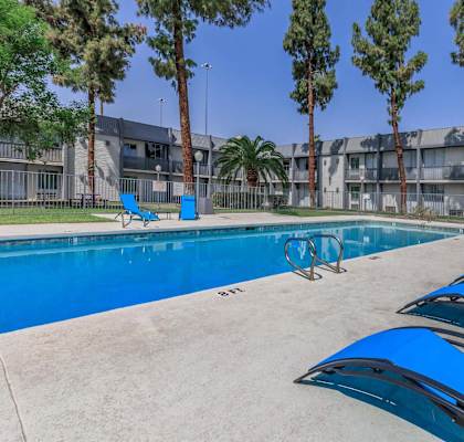A pool with blue chairs and trees in front of a building.