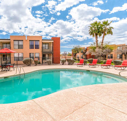 A swimming pool in front of a building with a red umbrella.