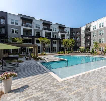 a swimming pool with lounge chairs and umbrellas in front of an apartment building  at Century University City, Charlotte, 28213