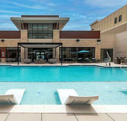 a swimming pool with lounge chairs and umbrellas in front of a building at Century West Pryor, Lee's Summit, MO