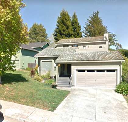 A house with a grey garage door is surrounded by greenery.
