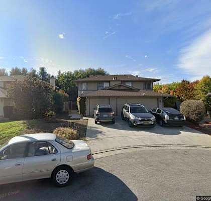 A silver car is parked in a driveway with a house and other cars in the background.