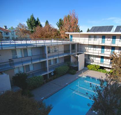 A high sky view of the Aegena apts inner courtyard with a pool the beige building wraps around the pools with trees in the background Prodesse Property Group 1211 Garbo Way  San Jose, CA 95117