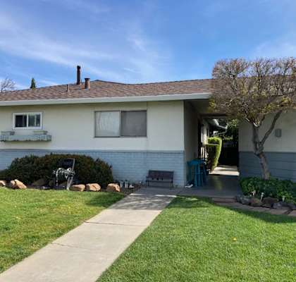 A house with a white exterior and a brown roof with a tree in front.
