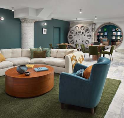 Commonwealth Vault Lounge with a white sofa, a blue armchair, and a wooden coffee table with converted bank vault in the background featuring a listening room.