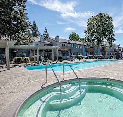 A hot tub sits in the middle of a pool area with a building in the background at Sierra Glen Apartments, California, 95621