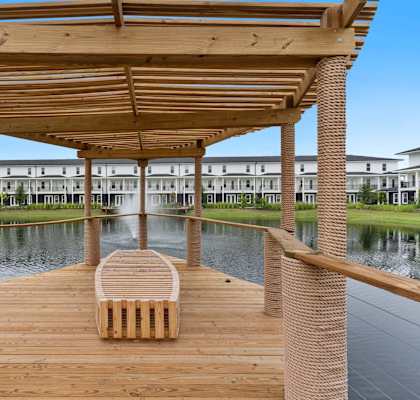 A wooden bench sits under a wooden pergola by a body of water.