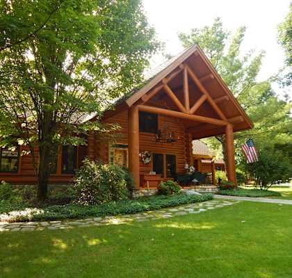 the front of a log cabin with a lawn and trees