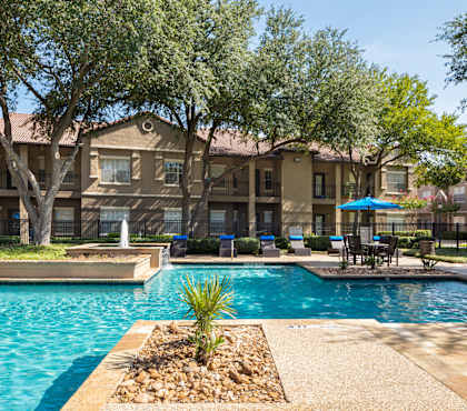 A swimming pool surrounded by trees and a building in the background.
