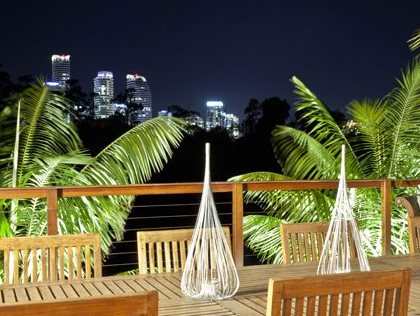 A wooden table and chairs are set up on a balcony with a view of a city skyline at night.