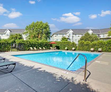 The turquoise outdoor pool with pool chairs, tables, and chairs with the apartments in the background at Heritage Park. 