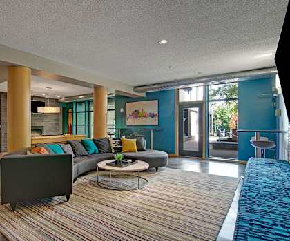 The resident lounge with turquoise walls and pillows, couches, decorations, plush chairs, coffee tables, and French doors to the pool area at Marbella on Dean Apartments. 