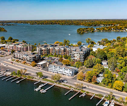 An arial view of the Mist at Lake Minnetonka with a view of the road and the harbor on Lake Minnetonka with trees on the lake at the Mist on Lake Minnetonka Apartment Homes. 