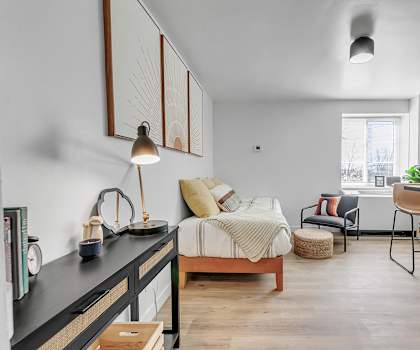 A bedroom with a bed, chair, and a plant.
