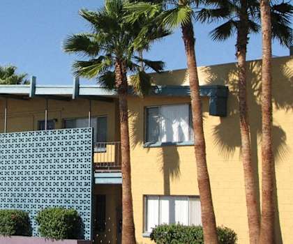a yellow building with a green lattice facade and palm trees in front of it
