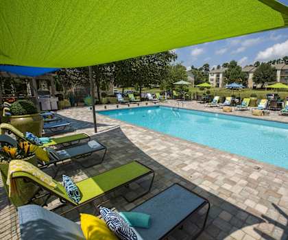 A pool area with a green umbrella and lounge chairs.