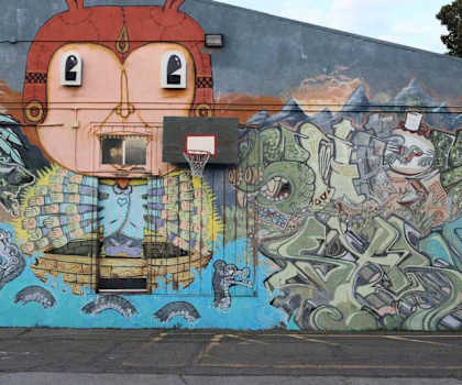 A mural of a face with a basketball hoop for a mouth is painted on a wall.