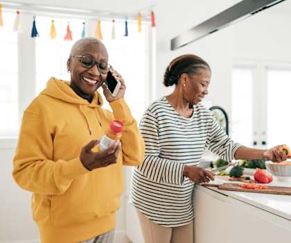 an older woman talking on a cell phone while preparing food with an older  woman at 55+ Remington at Ladera Ranch, Ladera Ranch, 92694