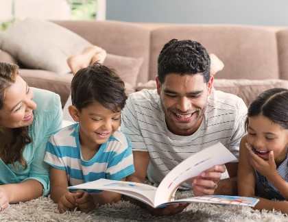 A family of four is lying on the floor and reading a book together.