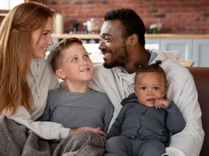 A family of four is sitting together on a couch.