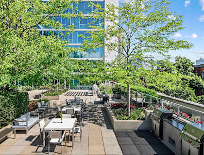 a patio with tables and chairs and trees and a building in the background at Halsted Flats Apartments, Chicago, IL, 60613