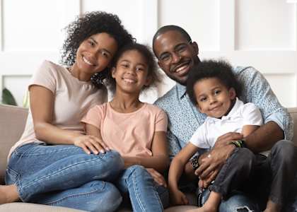 A family of four is sitting closely together on a couch.