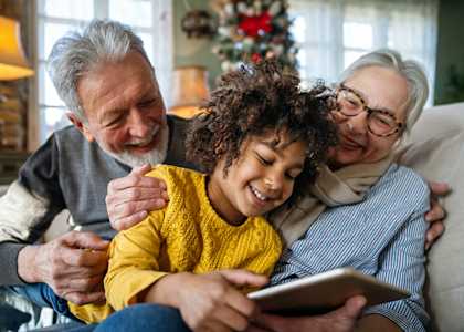 A family of three is sitting on a couch with a tablet in the middle person's hands.