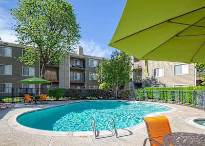 A swimming pool surrounded by chairs and umbrellas in front of a building.