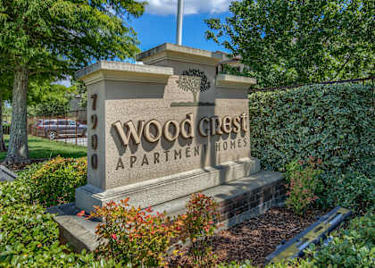 A stone sign for Woodcrest Apartments is surrounded by greenery.