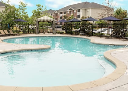 A large outdoor swimming pool surrounded by a black fence and umbrellas at Broadstreet at EastChase Apartments, Montgomery, Alabama