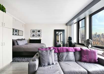 A room with a couch, a bed, a lamp, a plant, and a view of the city.