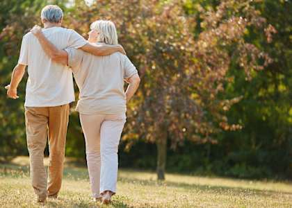 an older man and woman walking through a park
