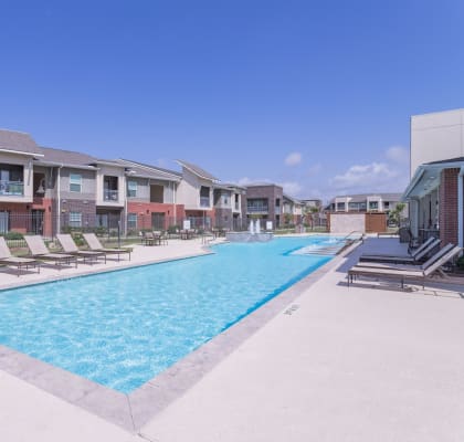 a swimming pool with lounge chairs and apartments in the background at Century Palm Bluff, Portland, TX, 78374