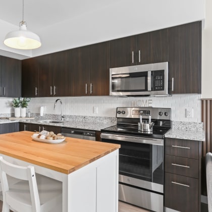 a kitchen with dark cabinets and a white island with two white chairs