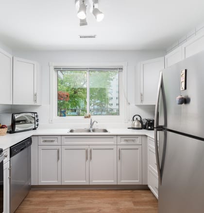 a white kitchen with stainless steel appliances and a window