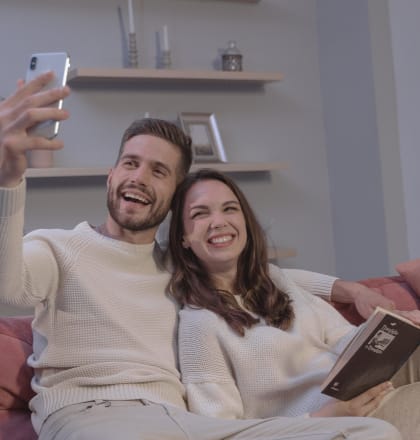 a couple sitting on a couch taking a photo of themselves with their phone