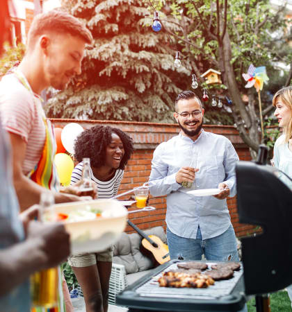 a group of people standing around a bbq at a backyard party