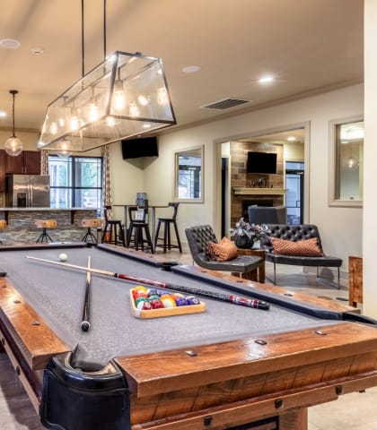 a pool table in a clubhouse with a kitchen in the background