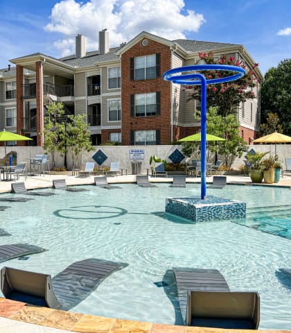 a swimming pool with lounge chairs and umbrellas in front of a building  at Quail Ridge Apartment Homes, Bartlett, TN