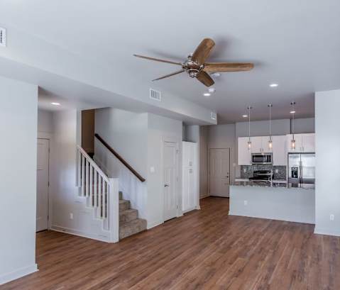 a living room with a ceiling fan and a kitchen in the background