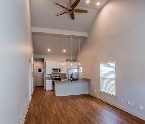 a living room with a ceiling fan and a kitchen in the background