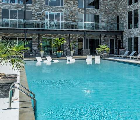 a large swimming pool with lounge chairs and a stone building in the background