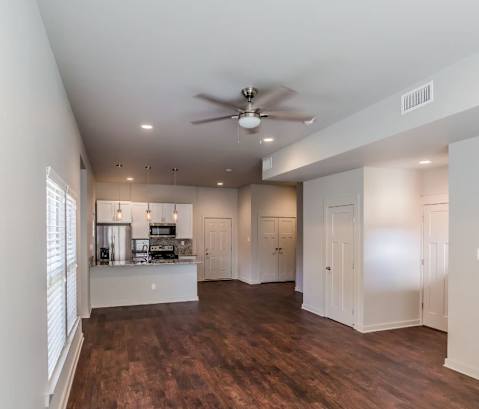 a living room with a ceiling fan and a kitchen in the background