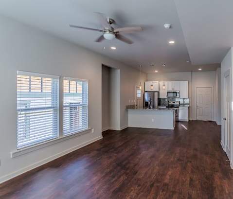 a living room with a ceiling fan and a kitchen in the background