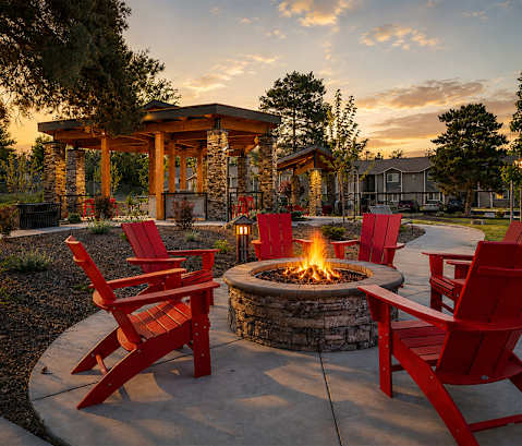 A fire pit surrounded by red chairs in a garden.