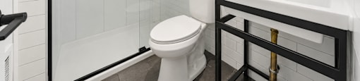 A white toilet sits in a bathroom with a black and white tile wall.