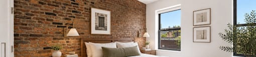 A bedroom with a brick wall and a bed with a white comforter.